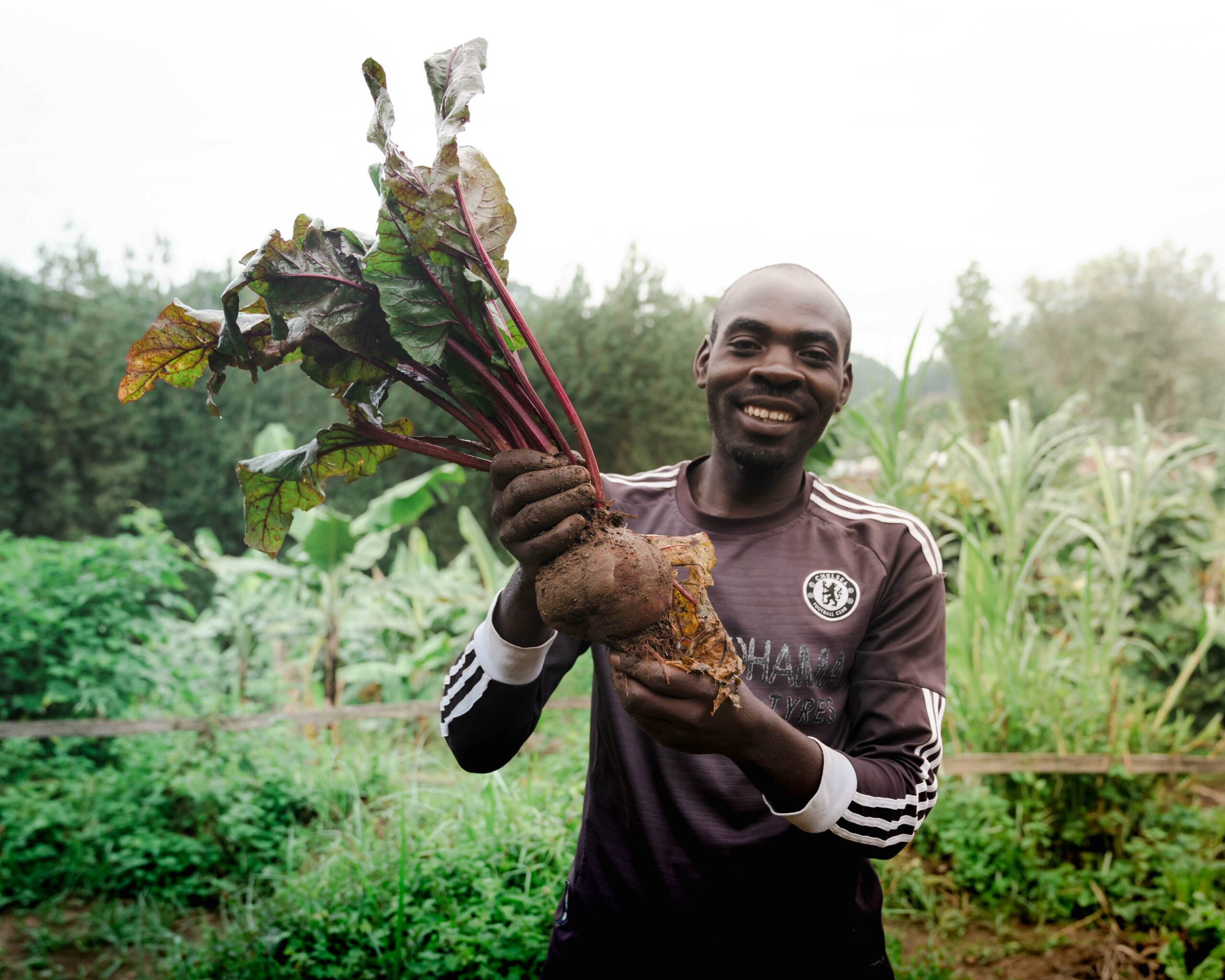 alt="smiling staff in garden holding a locally grown garden vegetable"