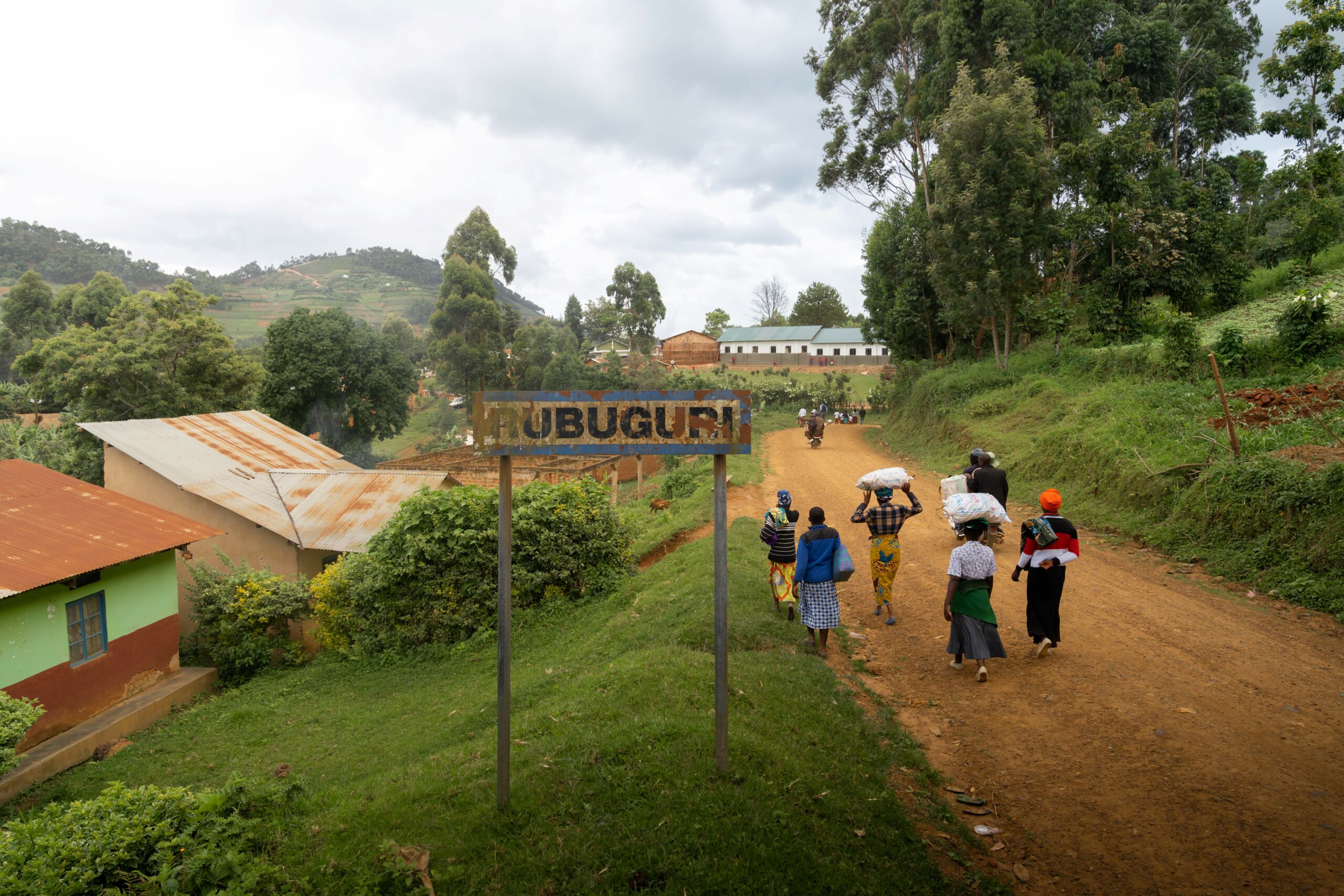 alt="image of locals walking on a road with a Rubuguri sign on the side of the road"